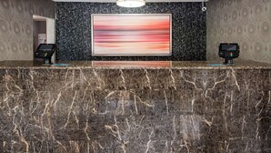 A marble reception desk with two digital kiosks, a large abstract painting, and patterned wallpaper.