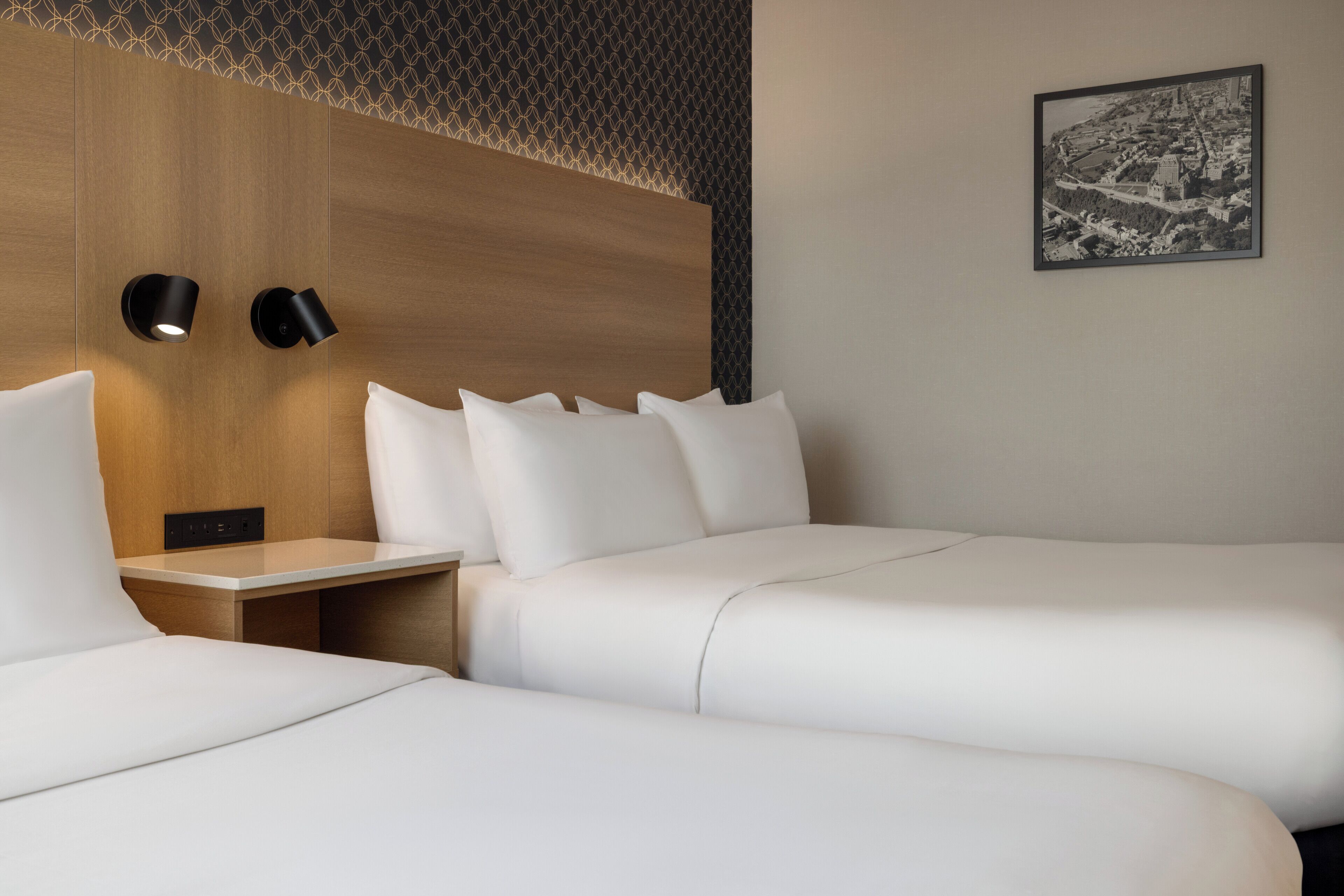 Een hotelkamer met twee bedden, een houten hoofdbord en een zwart-wit foto van een stadsgezicht aan de muur.
