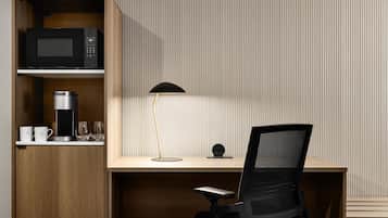 A modern office space with a wooden desk, a black office chair, a black lamp, a coffee maker, and a microwave on a shelf.