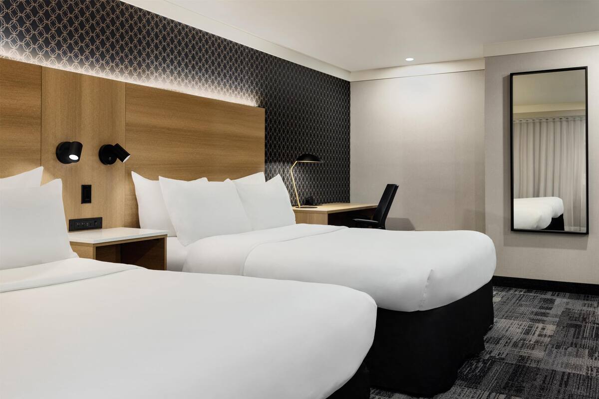 A hotel room with two beds, a desk, a chair, a mirror, and a patterned wall.