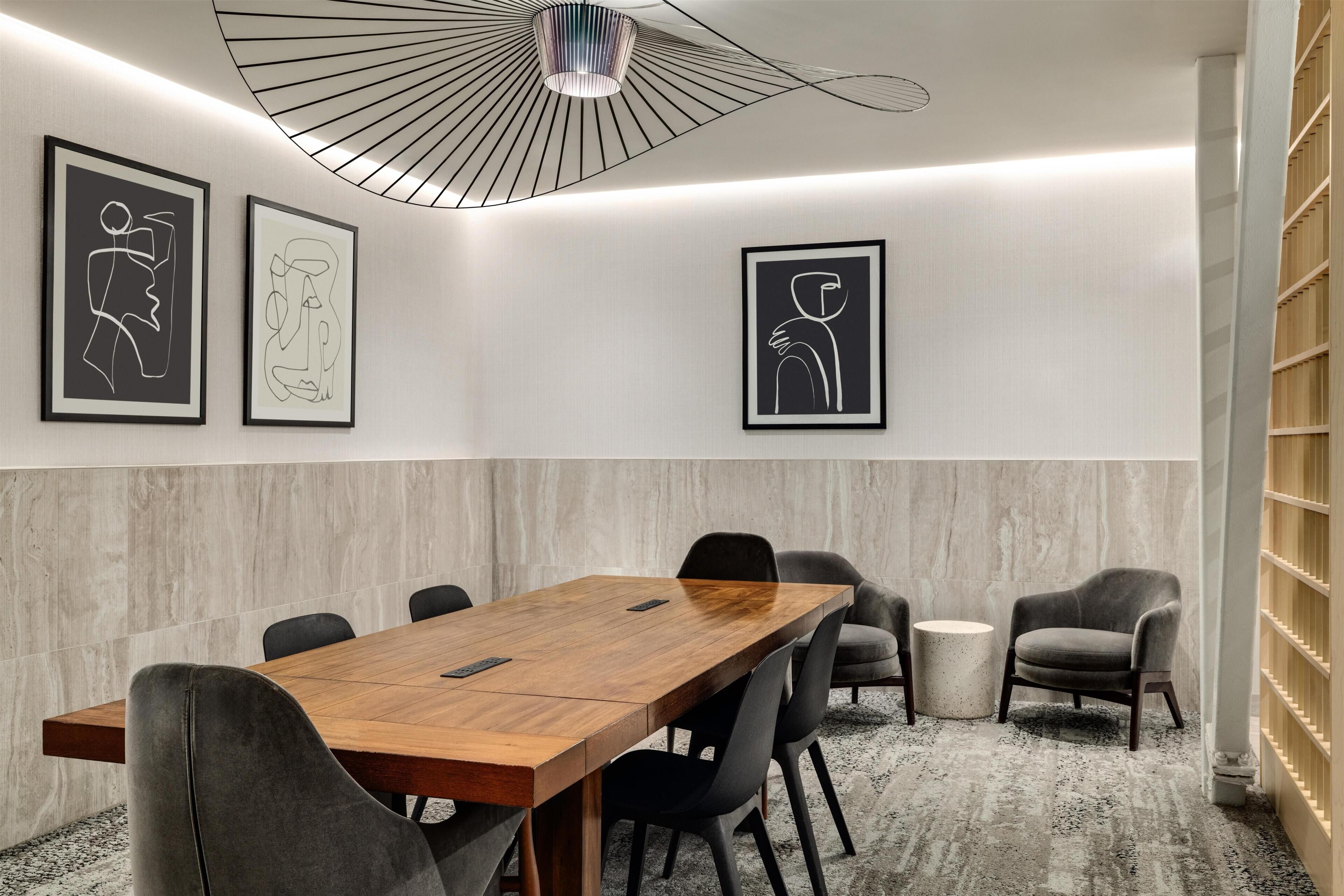 A conference room with a wooden table, black chairs, a round table, and a modern ceiling light fixture.