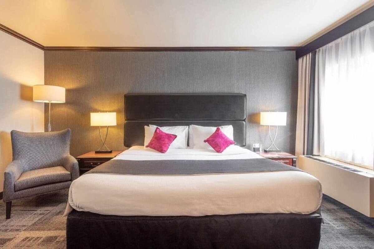 A hotel room with a large bed, two bedside lamps, a chair, and a window with curtains.