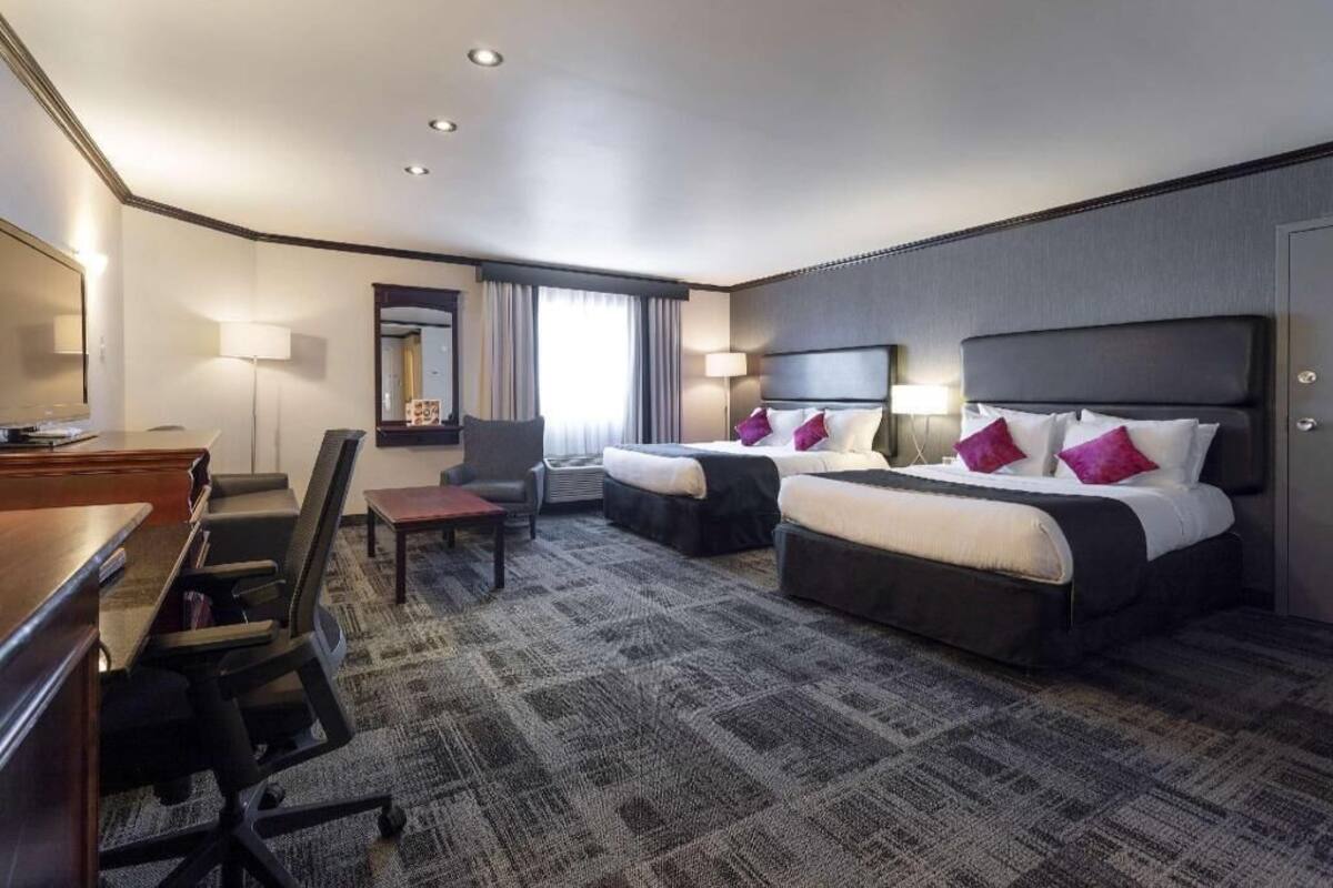 A hotel room with two beds, a desk, a chair, and a carpeted floor.