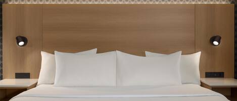 Habitación de hotel con cabecera de madera, dos mesitas de noche, ropa de cama blanca y lámparas de lectura fijadas a la pared.