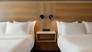 A hotel room with two beds, a wooden headboard, a small bedside table, and a wall-mounted light fixture.