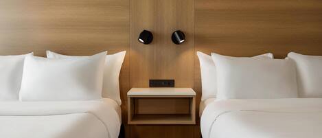 A hotel room with two beds, a wooden headboard, a small bedside table, and a wall-mounted light fixture.