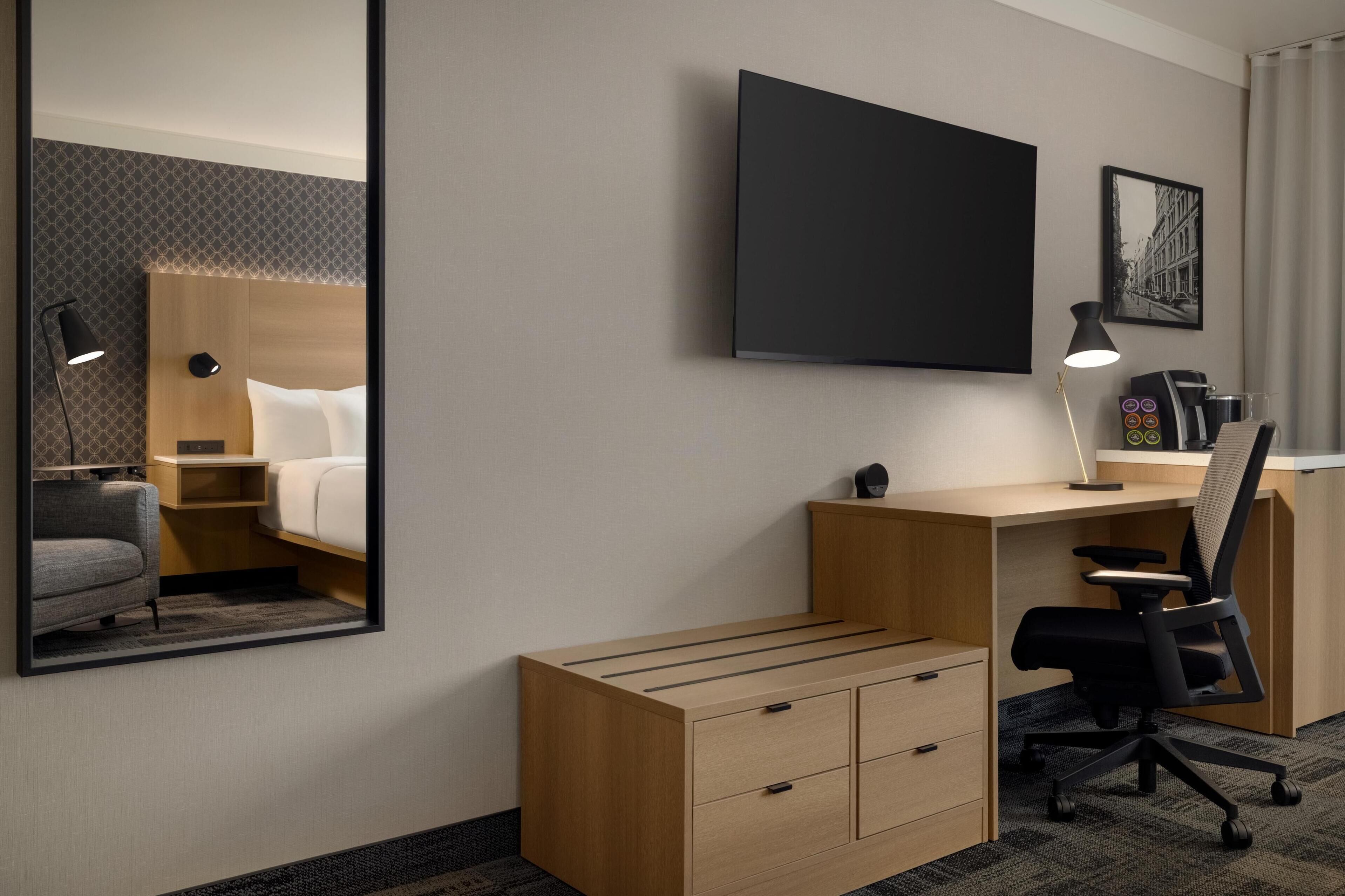 Habitación de hotel con cama, escritorio, silla, televisor y cafetera.
