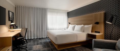 Una habitación de hotel con cama, escritorio, silla y un ventanal con cortinas.