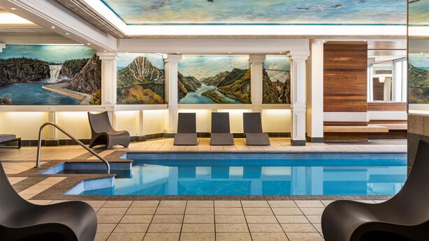 Una piscina interior moderna con un mural de un paisaje montañoso, sillones de descanso y un revestimiento de madera.