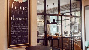 A café interior with a chalkboard sign, round tables, and a view through large windows.