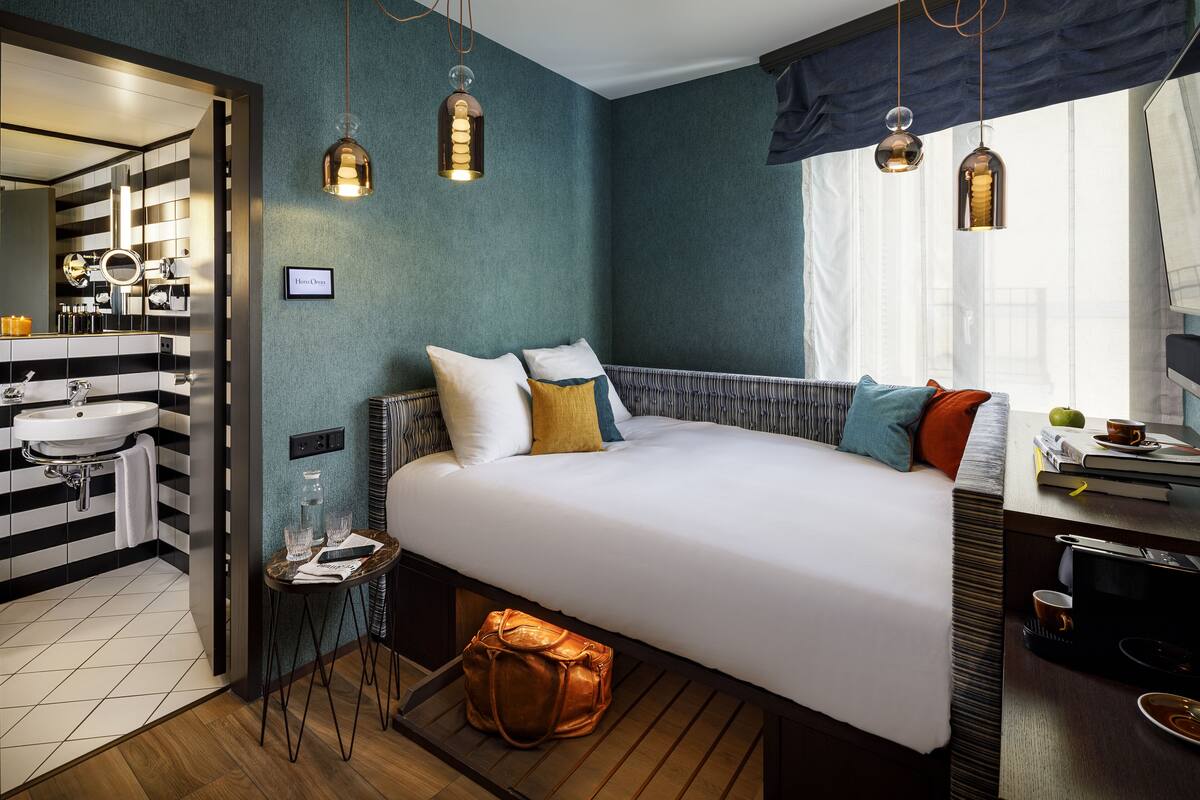 A modern hotel room with a bed, bedside table, and a bathroom with a sink and mirror.