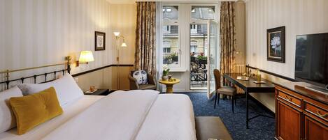A hotel room with a large bed, a desk, a chair, a television, and a view of the outside balcony.