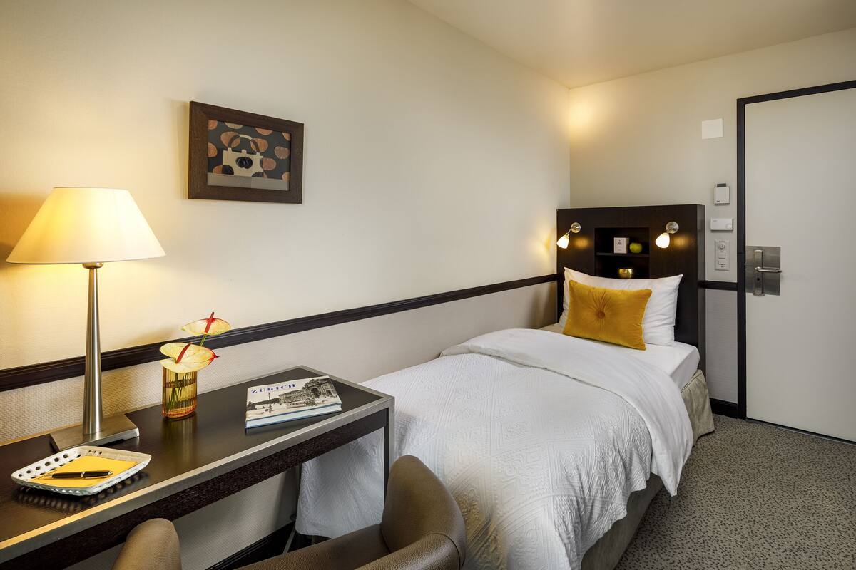 A hotel room with a bed, bedside table, lamp, and a framed picture on the wall.