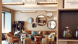 A modern lounge area with sofas, armchairs, and a coffee table, featuring a herringbone patterned wall and multiple mirrors.