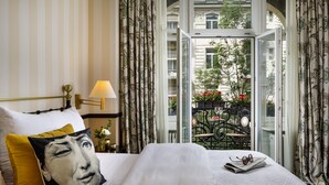 A hotel room with a bed, a nightstand, a lamp, and a view of the outside balcony.