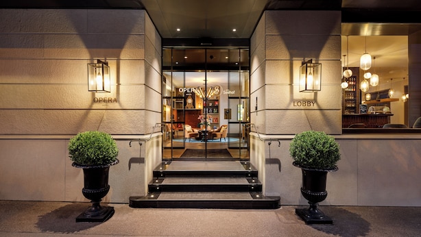 The entrance to a hotel with a lobby area, a staircase leading up to the lobby, and two potted plants on either side of the entrance.