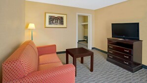 A hotel room with a sofa, a small table, a TV on a cabinet, and a framed picture on the wall. - Days Inn by Wyndham Silver Spring (Silver Spring)