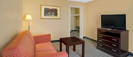 Habitació d'hotel amb un sofà, una taula petita, un televisor sobre un moble i un quadre amb marc a la paret.