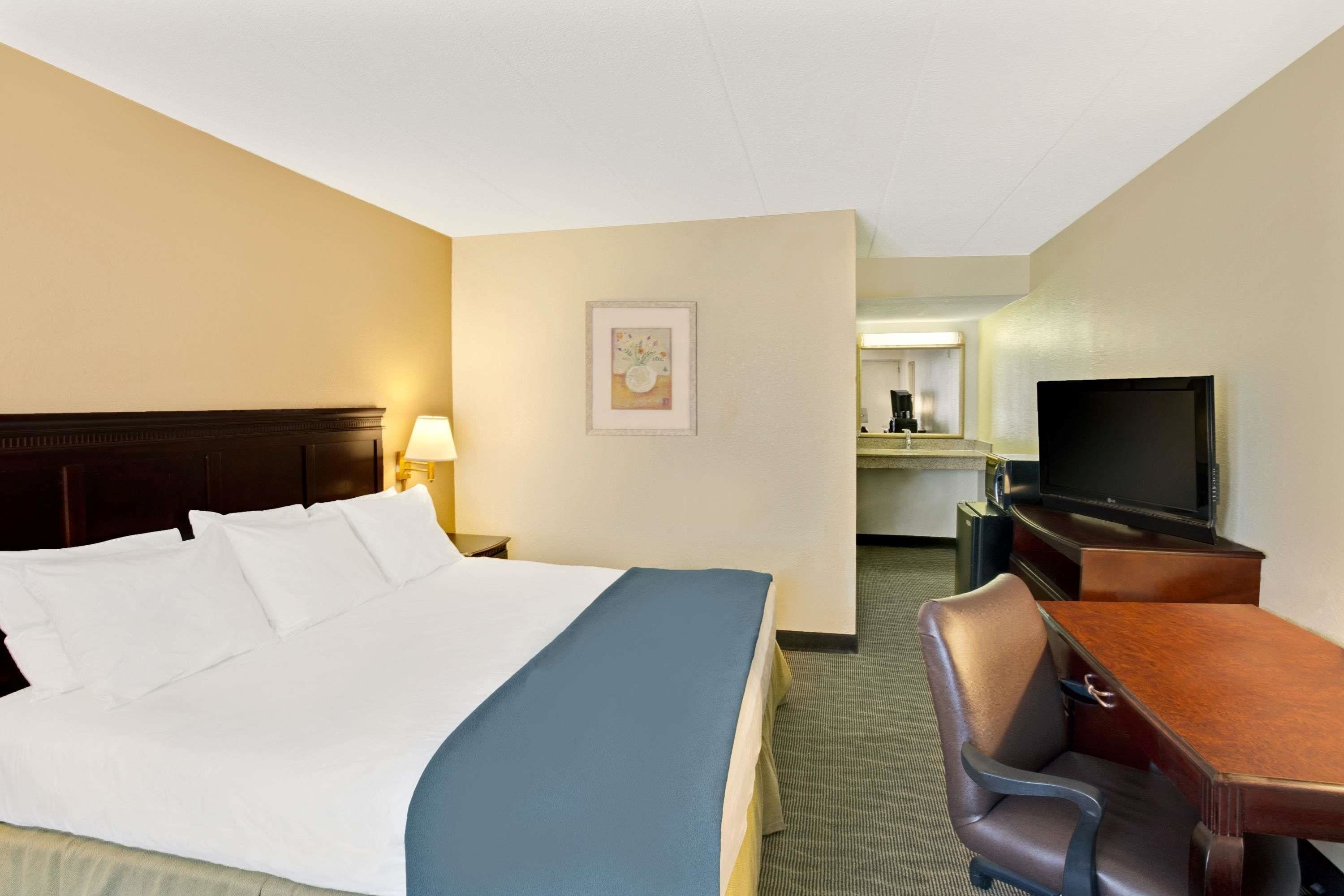 A hotel room with a bed, a desk, a chair, a television, and a framed picture on the wall.