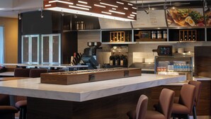 A modern restaurant interior with a central bar area, seating, and a menu display.