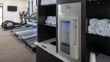 A gym with treadmills, a water dispenser, and neatly rolled towels on shelves.