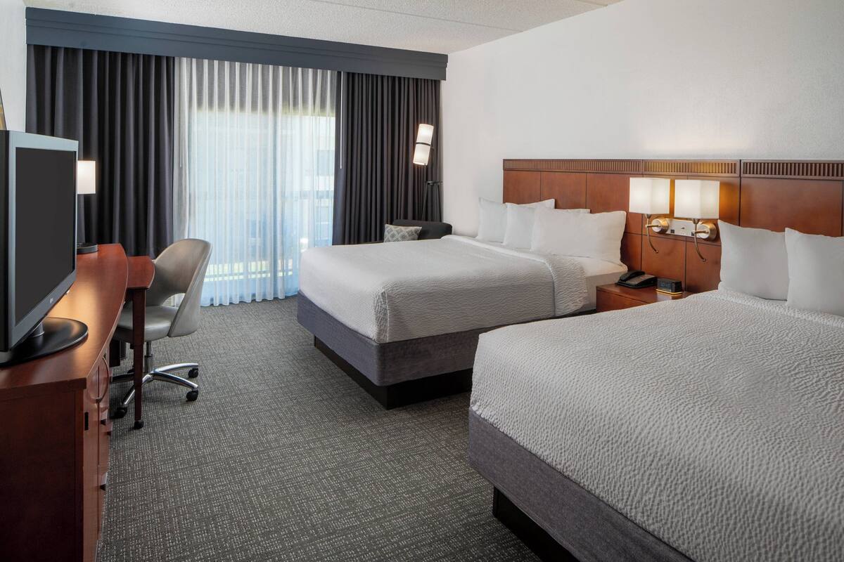 Ein Hotelzimmer mit zwei Betten, einem Schreibtisch mit Computer, einem Stuhl und einem Fernseher.