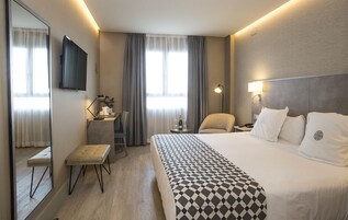 A hotel room with a large bed, a desk, a chair, a TV, and a lamp.