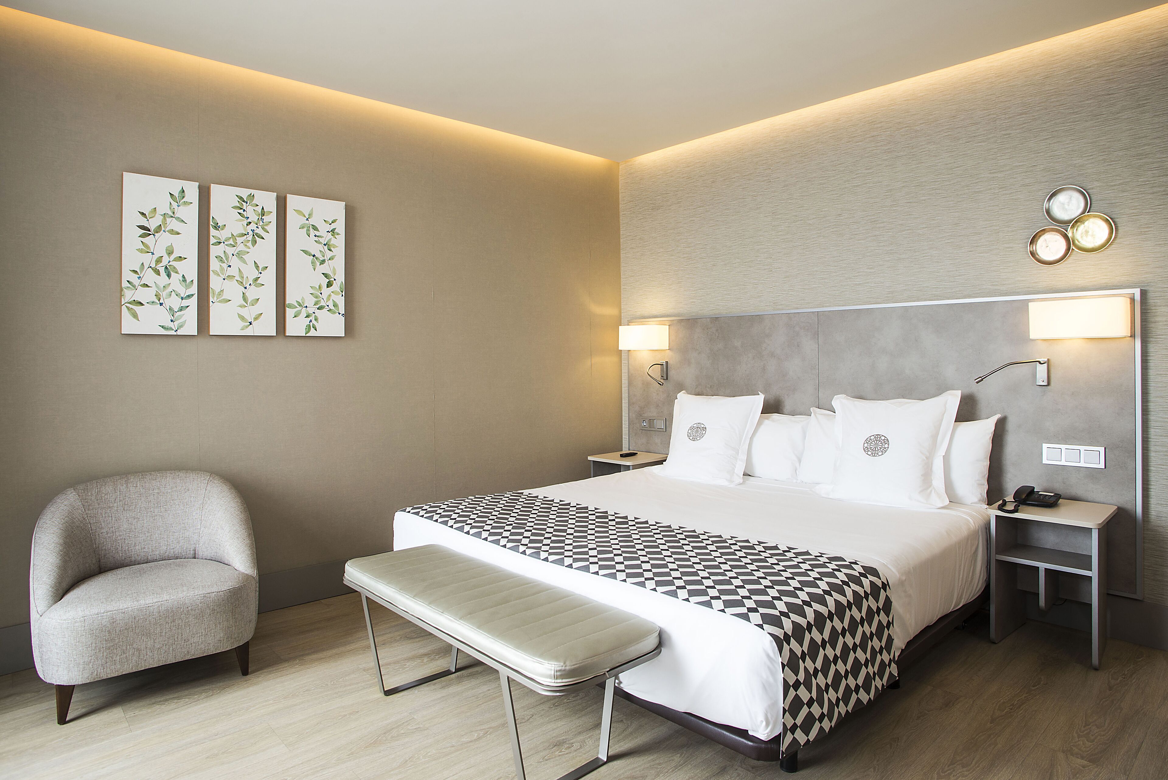 Une chambre d’hôtel moderne avec un grand lit, un banc, une chaise et des œuvres d’art accrochées au mur.
