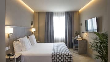 A hotel room with a bed, bedside table, lamp, desk, chair, and a TV.
