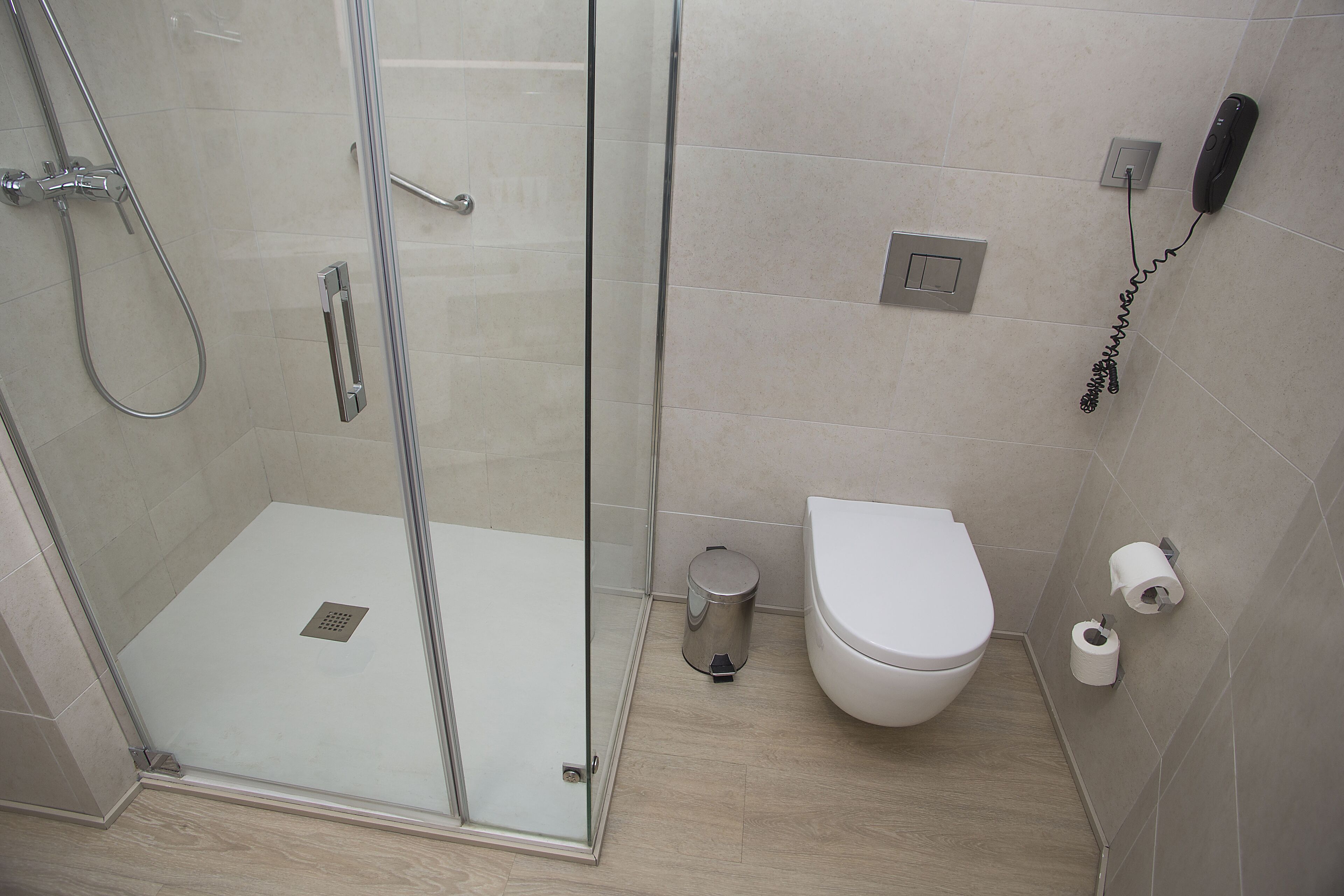 A bathroom with a glass-enclosed shower, a toilet, and a trash can.