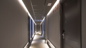 Un largo y estrecho pasillo de hotel con puertas a ambos lados, suelo alfombrado e iluminación en el techo.