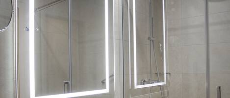 A modern bathroom with a large mirror, a shower enclosure, and a sink with two glasses.