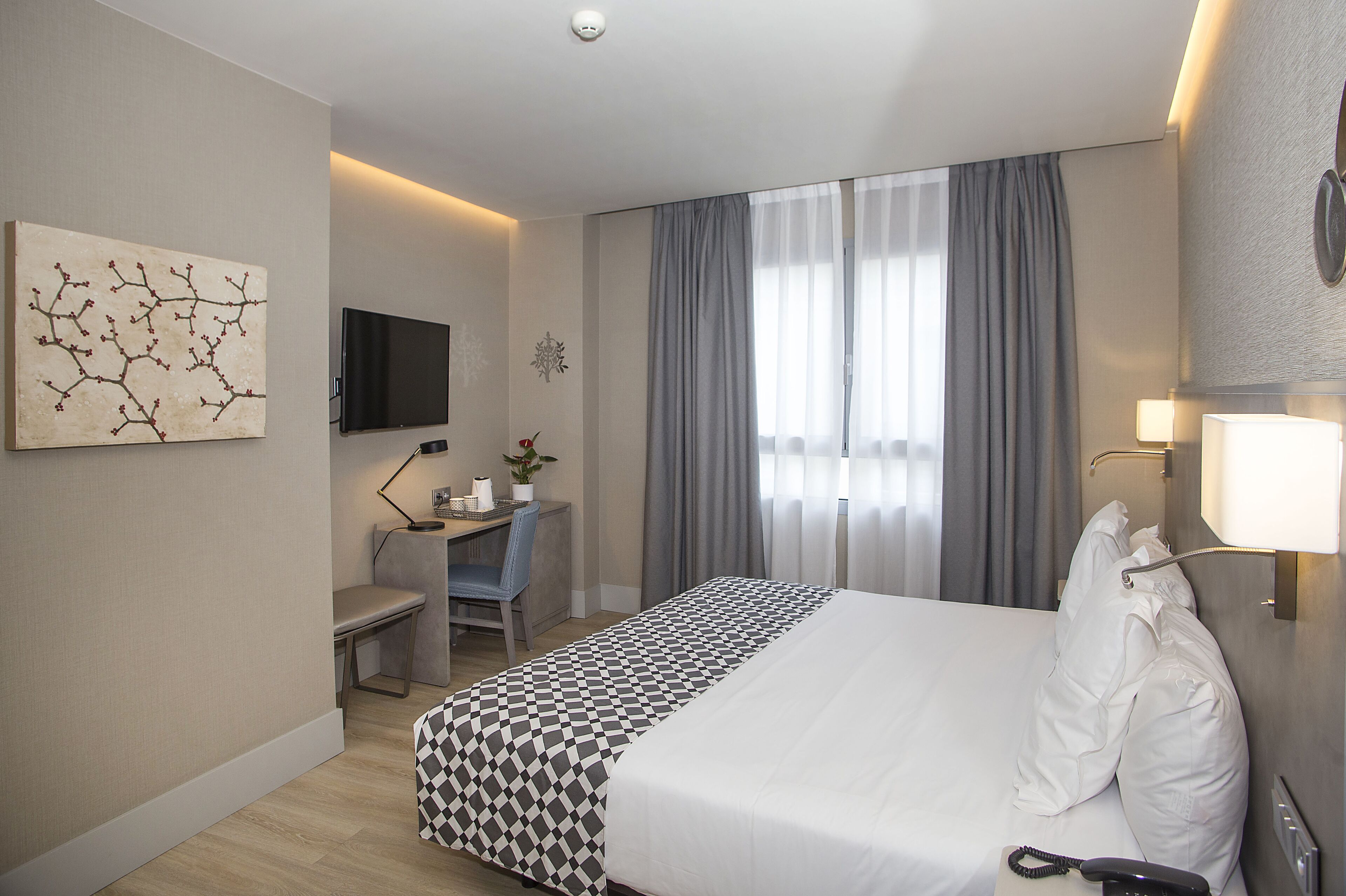 Une chambre d’hôtel avec un grand lit, un bureau avec une chaise, une télévision et une fenêtre avec des rideaux.