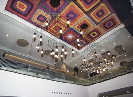A modern interior with a geometric ceiling design, multiple hanging light fixtures, and a visible staircase.