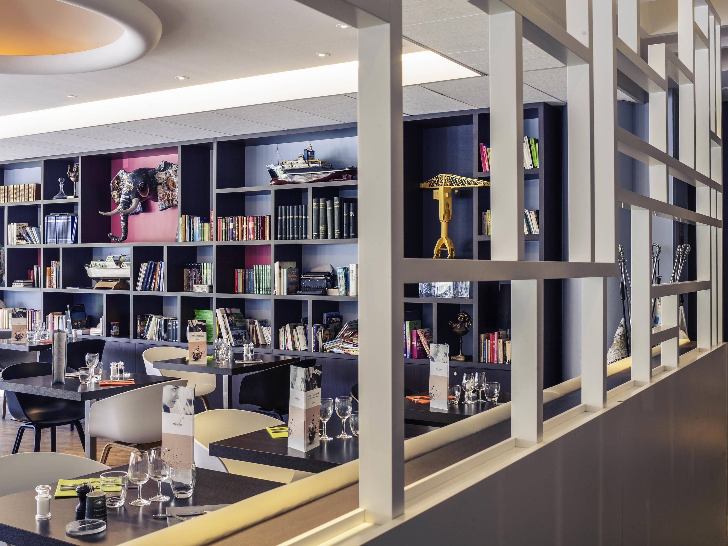 A modern library with bookshelves, a dining area, and a decorative sculpture.