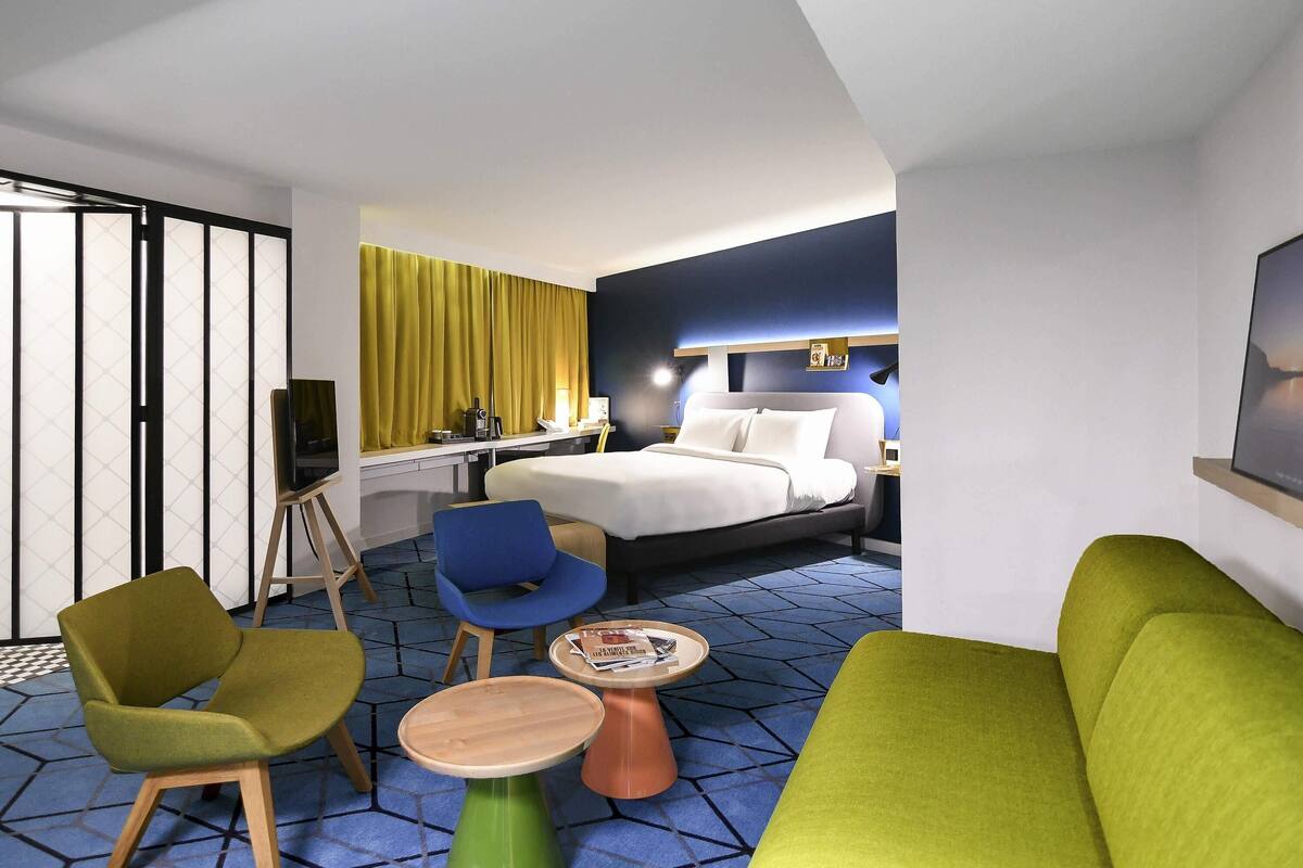 A modern hotel room with a bed, a desk, a chair, a sofa, and a small table.