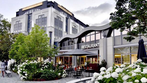 Een modern gebouw met een restaurant op de begane grond, terras en een voetpad.