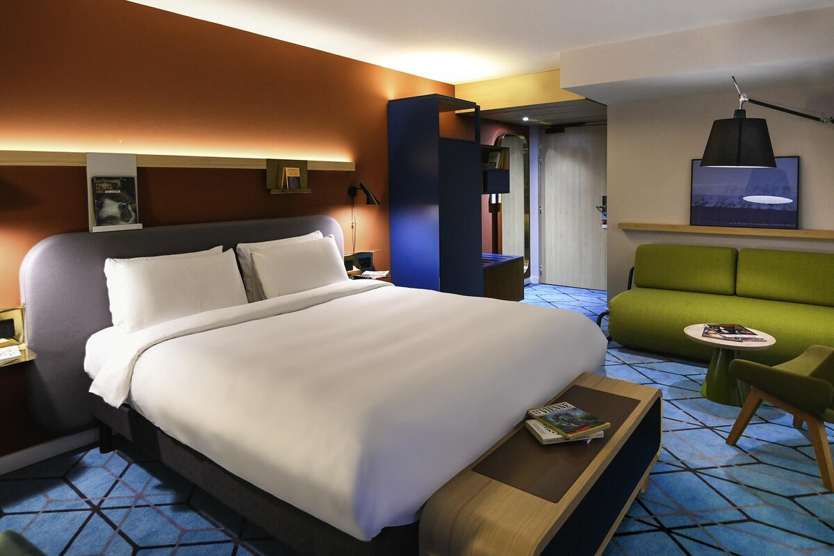 Une chambre d’hôtel avec un grand lit, un canapé vert, une petite table et un téléviseur fixé au mur.
