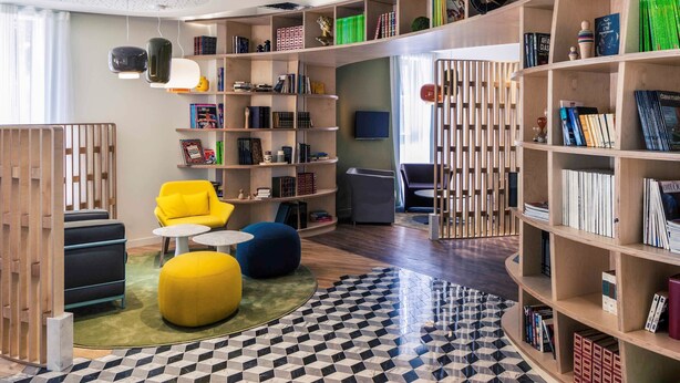 A modern library with bookshelves, a yellow chair, and a black and white patterned floor. - Mercure Nantes Centre Gare (Nantes)