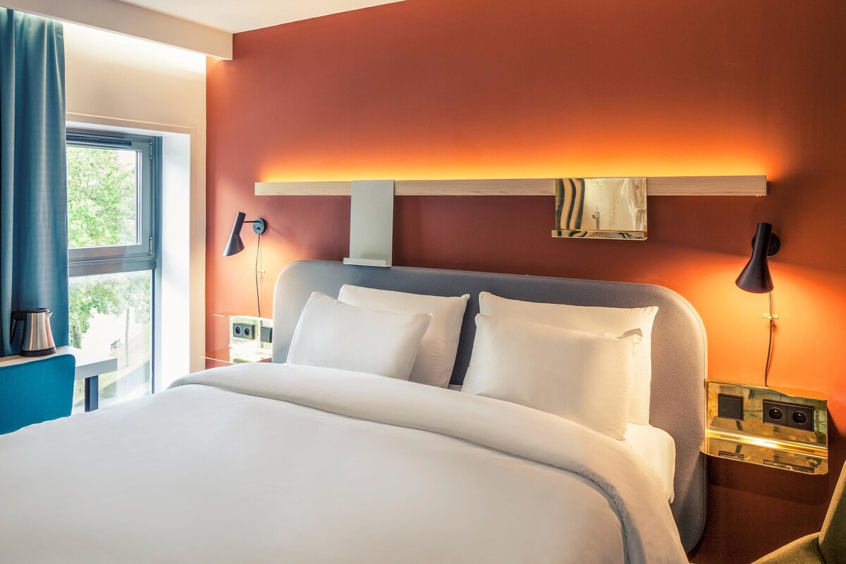 Une chambre d’hôtel avec un grand lit, deux lampes de chevet, une table de chevet et une fenêtre avec des rideaux.