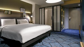Een moderne hotelkamer met een groot bed, een nachtkastje, een leeslamp en een inloopkast.