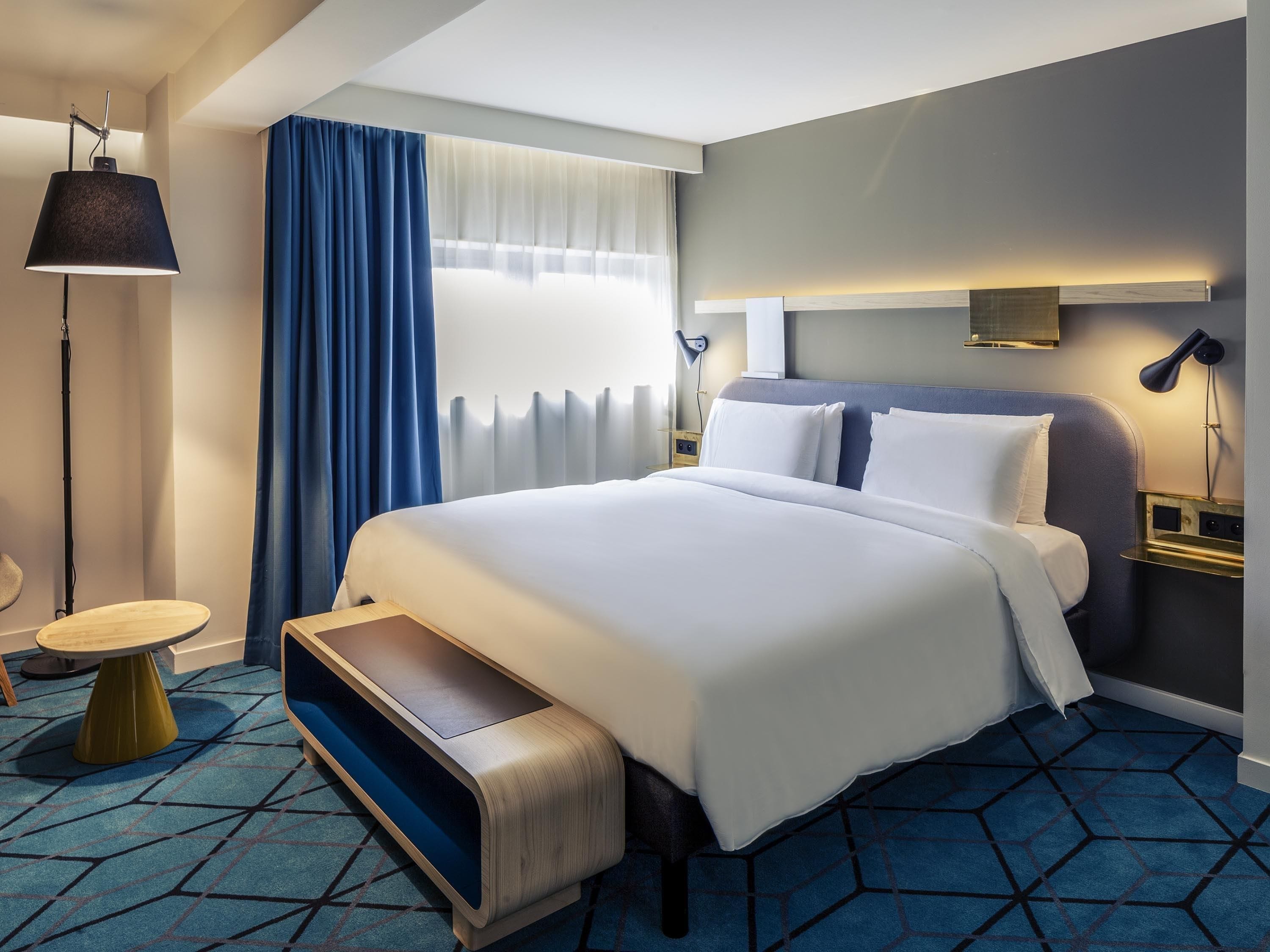 Une chambre d’hôtel moderne, dotée d’un grand lit, d’un bureau, d’une chaise et d’une lampe.