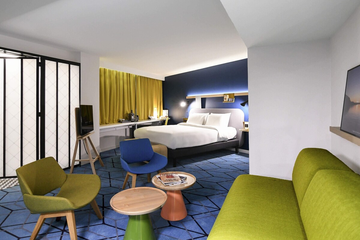 Een moderne hotelkamer met een bed, een bureau, een stoel, een bank en een kleine tafel.