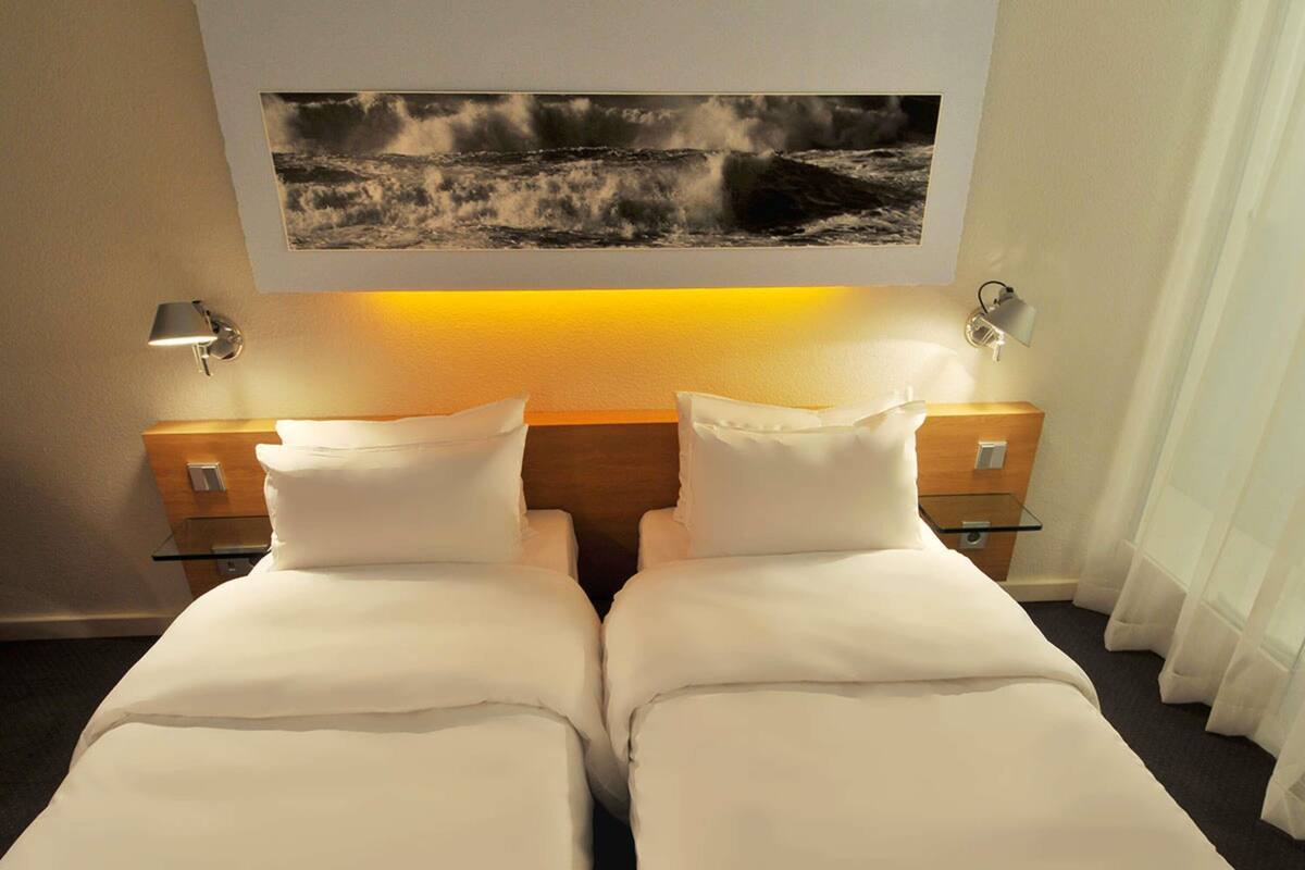 A hotel room with two beds, a nightstand, a lamp, and a framed picture above the beds.