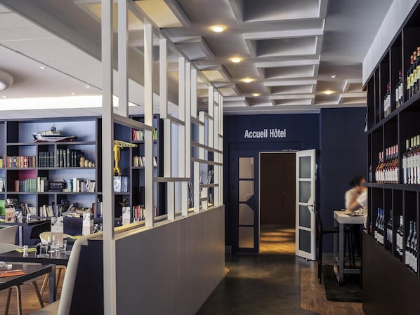 A hotel lobby with a reception desk, a bookshelf with books and decorative items, and a wine display.