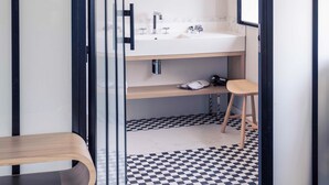 A modern bathroom with a checkered floor, a wooden bench, and a white sink with a mirror above it. - Mercure Nantes Centre Gare (Nantes)