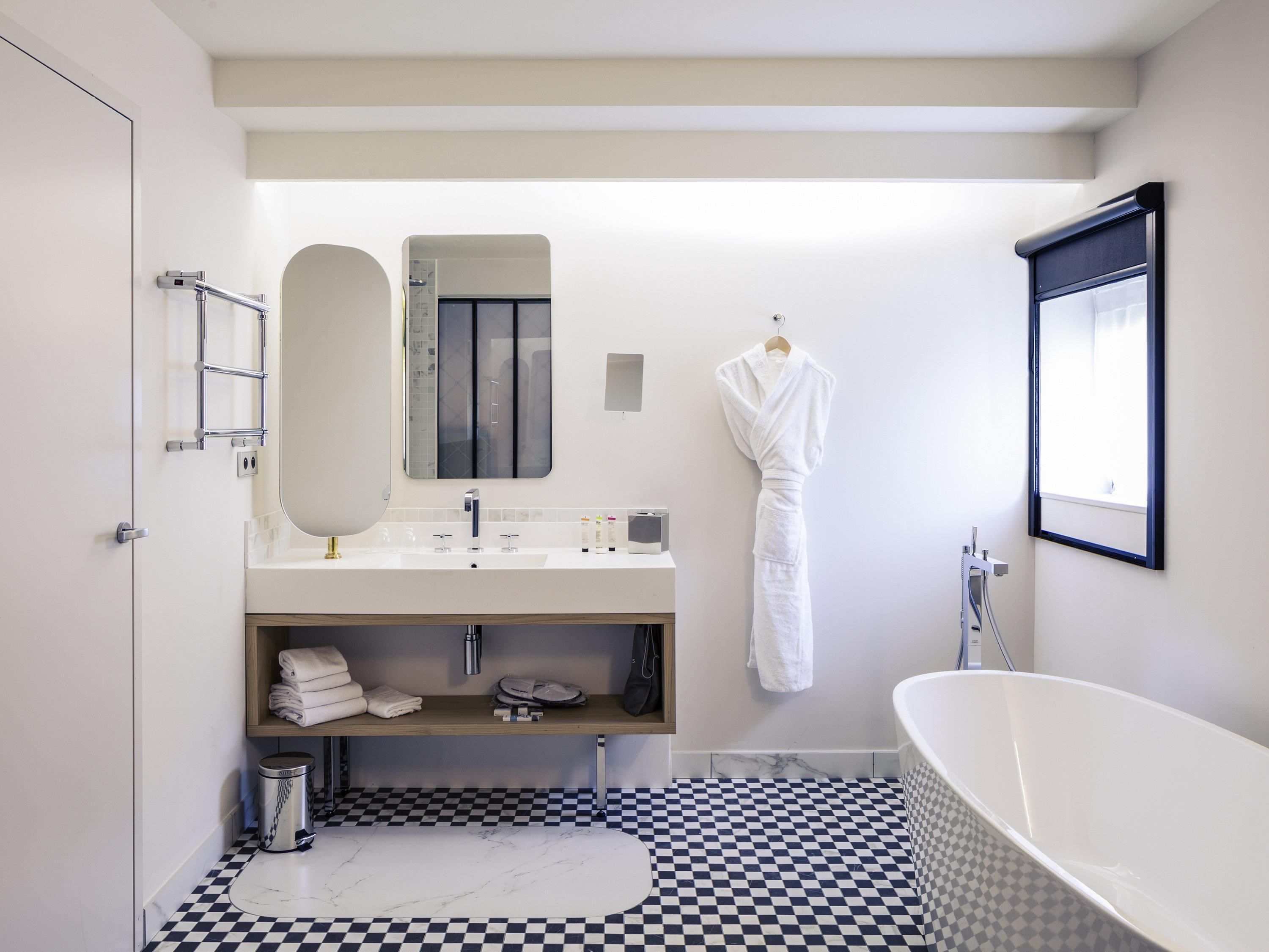 A modern bathroom with a checkered floor, a white bathtub, a vanity with a mirror, and a hanging robe.
