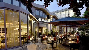 An outdoor dining area with tables and chairs, a restaurant building in the background, and a modern architectural design. - Mercure Nantes Centre Gare (Nantes)