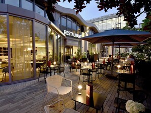 Un espace de restauration en plein air avec des tables et des chaises, un bâtiment de restaurant en arrière-plan et un design architectural moderne.