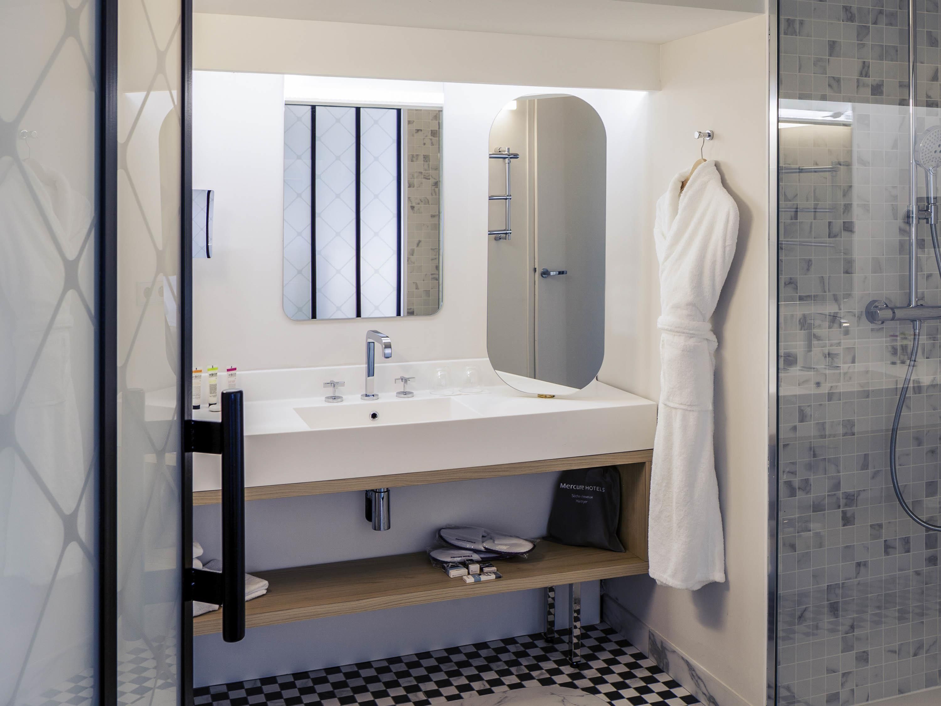 Un baño moderno con un lavabo blanco, un espejo grande, una bata colgada en la pared y una zona de ducha.